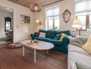 A cozy living room with a teal sofa, a wooden coffee table, and a painting on the wall. - 8 Person Holiday Home in Rudkobing (Rudkobing)