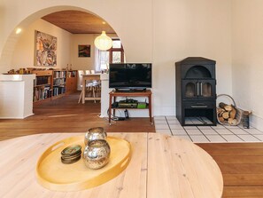A living room with a wooden floor, a TV, a fireplace, and a dining area with chairs and a table. - 8 Person Holiday Home in Rudkobing (Rudkobing)