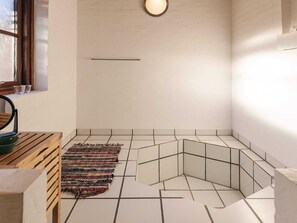 A bathroom with a wooden bench, a woven rug, and a geometric tile pattern on the floor.