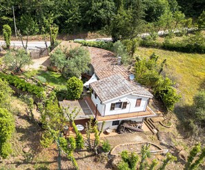 Een wit huis met pannendak, omringd door groen en een omheinde tuin.
