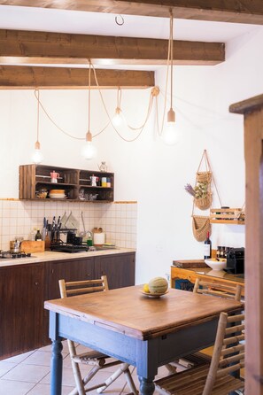 Een keuken met houten kastjes, een houten eettafel, hangende lampen en een macramé wanddecoratie.