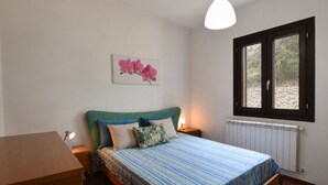 Une chambre à coucher comprenant un lit, une table de chevet, une lampe, un radiateur et une fenêtre donnant sur un paysage verdoyant.