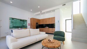 Un saló modern amb un sofà, una taula de centre rodona i una zona de cuina al fons.