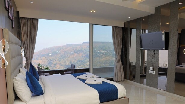 A modern hotel room with a large bed, a TV, and a view of the mountains.