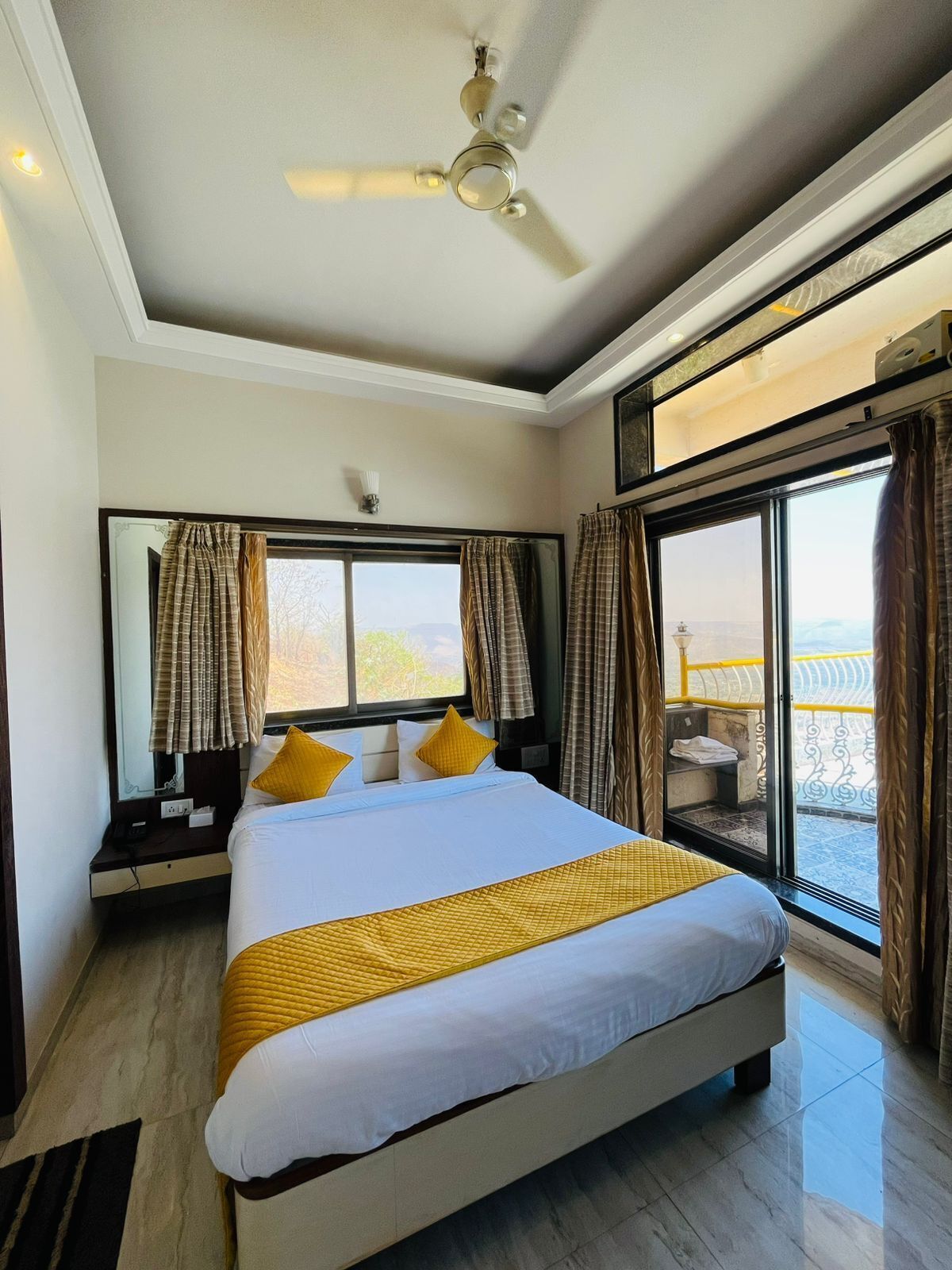 Une chambre d’hôtel avec un grand lit, un ventilateur de plafond, une fenêtre avec des rideaux et une vue sur l’extérieur.