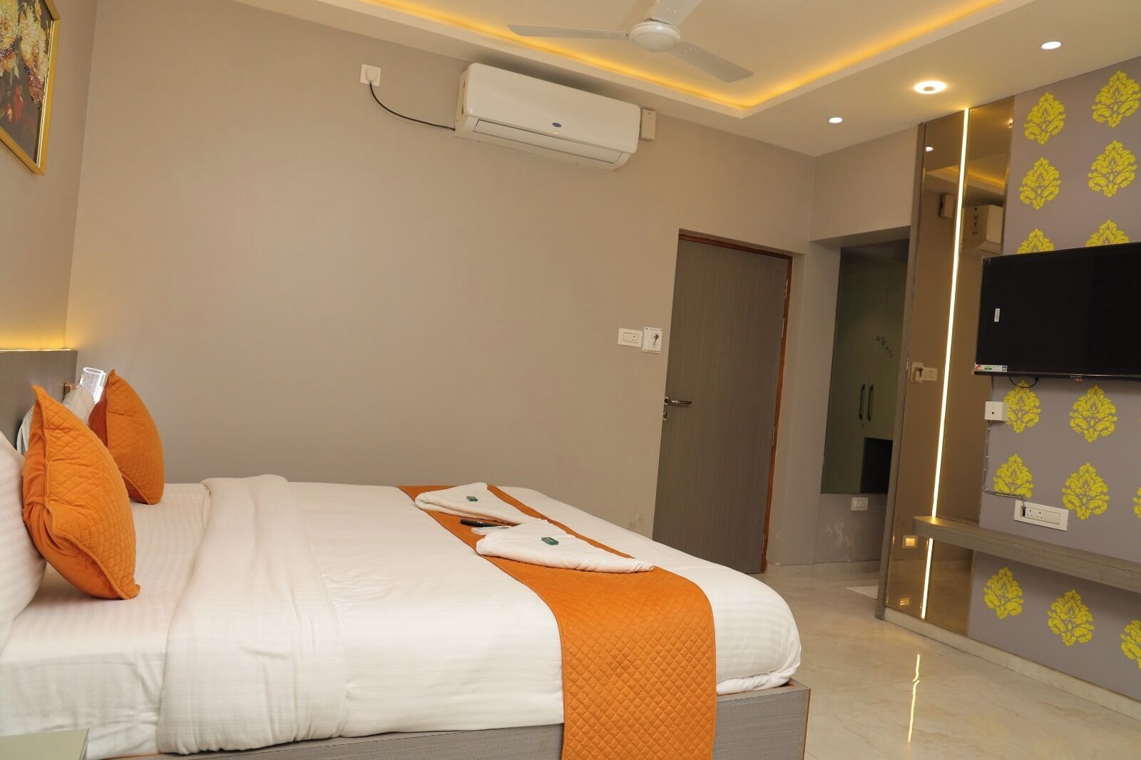 A hotel room with a bed, an air conditioning unit, a television, and a door.
