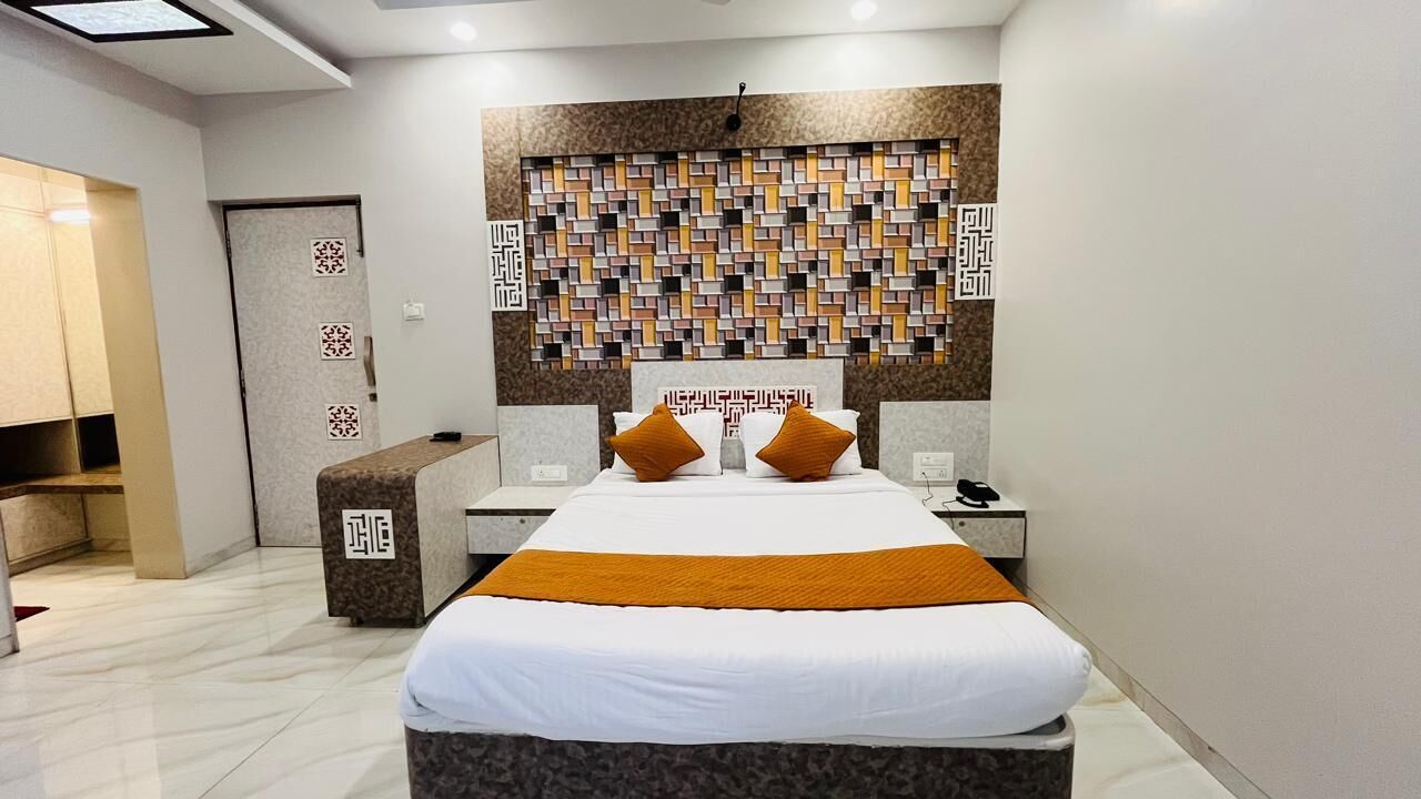 A modern hotel room with a large bed, two bedside tables, a decorative wall panel, and a reception desk.