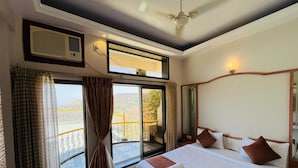 A hotel room with a large bed, a ceiling fan, a window with curtains, and a balcony with a railing.