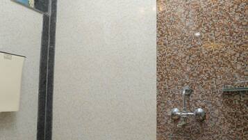 A bathroom with a toilet, a shower with a tiled wall, and a bucket.