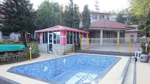 A swimming pool with a tiled deck, a small pavilion, and a fenced area.