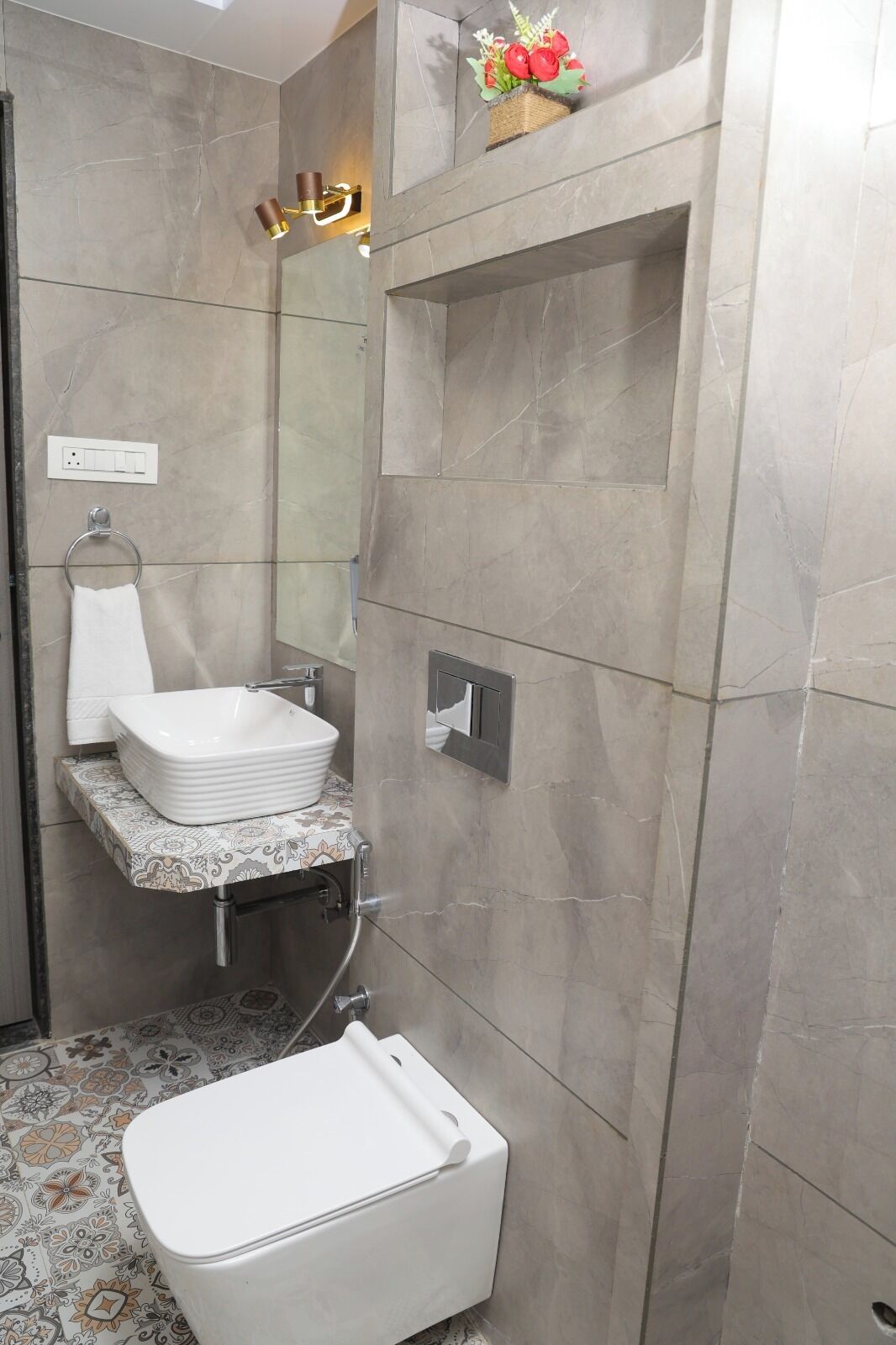 Une salle de bain avec un lavabo blanc, un miroir, un porte-serviettes, une douche et un arrangement floral décoratif.