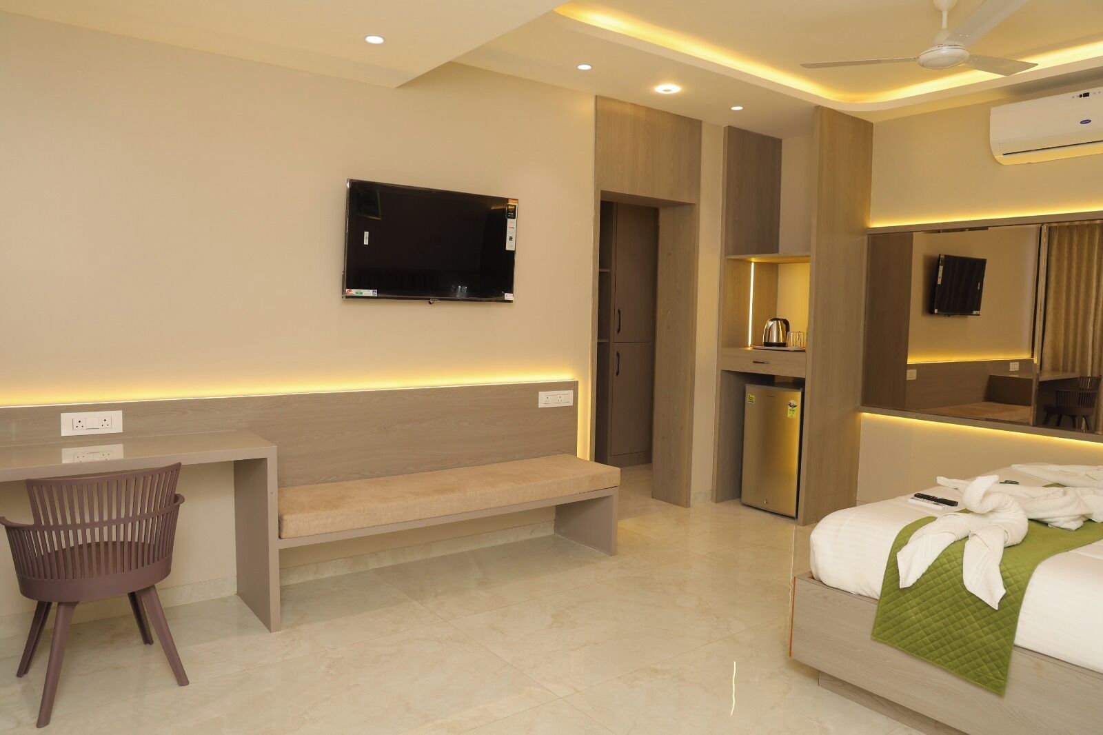 A hotel room with a bed, a desk, a chair, a television, a mini-fridge, and a mirror.