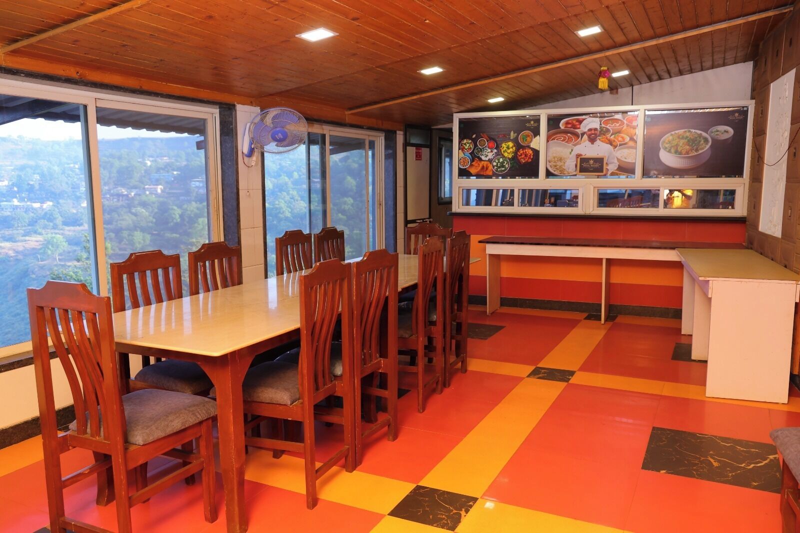 Un comedor con una mesa y sillas de madera, suelo a cuadros y vistas amplias a través de grandes ventanas.