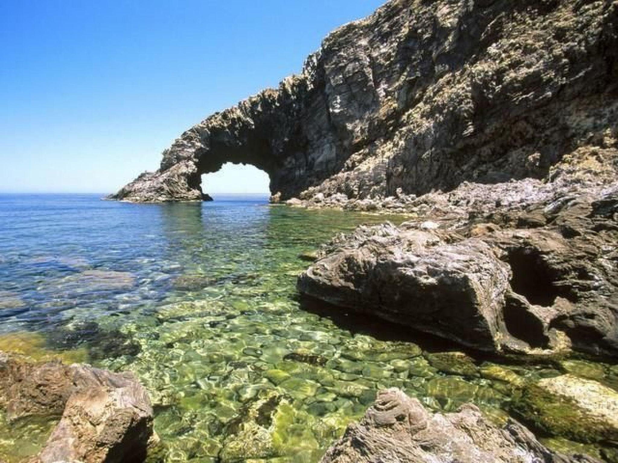 Paesaggio costiero roccioso con acque cristalline e un arco naturale.