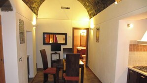 Un corridoio stretto con zona pranzo, tavolo e sedie, televisione e bagno con lavandino e specchio.