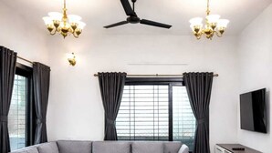 A modern living room with a sectional sofa, a coffee table, a TV, and a ceiling fan. - Taaffeite Hotel And Resorts (Pune)