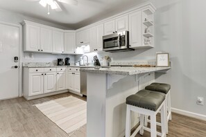 Una cocina con armarios blancos, microondas de acero inoxidable, cafetera y un taburete de bar.