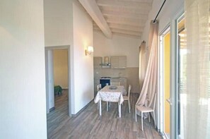 Une pièce comprenant une table à manger, des chaises, un coin cuisine et une porte-fenêtre coulissante.