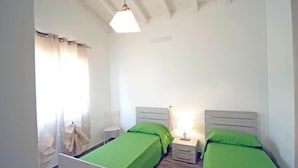 A room with two single beds, a nightstand with a lamp, a chair, and a window with curtains. - Villa Artemis apartment 1 (Capoliveri isola d'Elba)