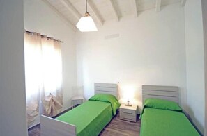 Une chambre avec deux lits simples, une table de chevet avec une lampe, une chaise et une fenêtre avec des rideaux.