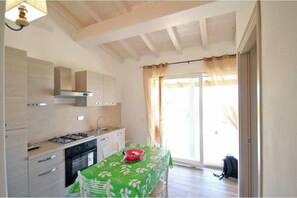 A kitchen with a gas stove, oven, and sink, a dining table with a green tablecloth, and a sliding glass door leading outside. - Villa Artemis apartment 2 (Capoliveri isola d'Elba)