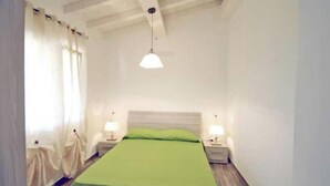 Une chambre à coucher avec un lit, des tables de chevet, une lampe suspendue et une fenêtre avec des rideaux.