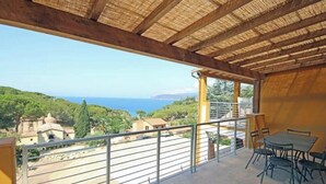 Un balcon avec vue sur la mer, une table avec des chaises et un toit de chaume.