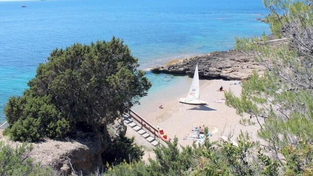 Une plage côtière avec un voilier, une côte rocheuse et une vue dégagée sur la mer.