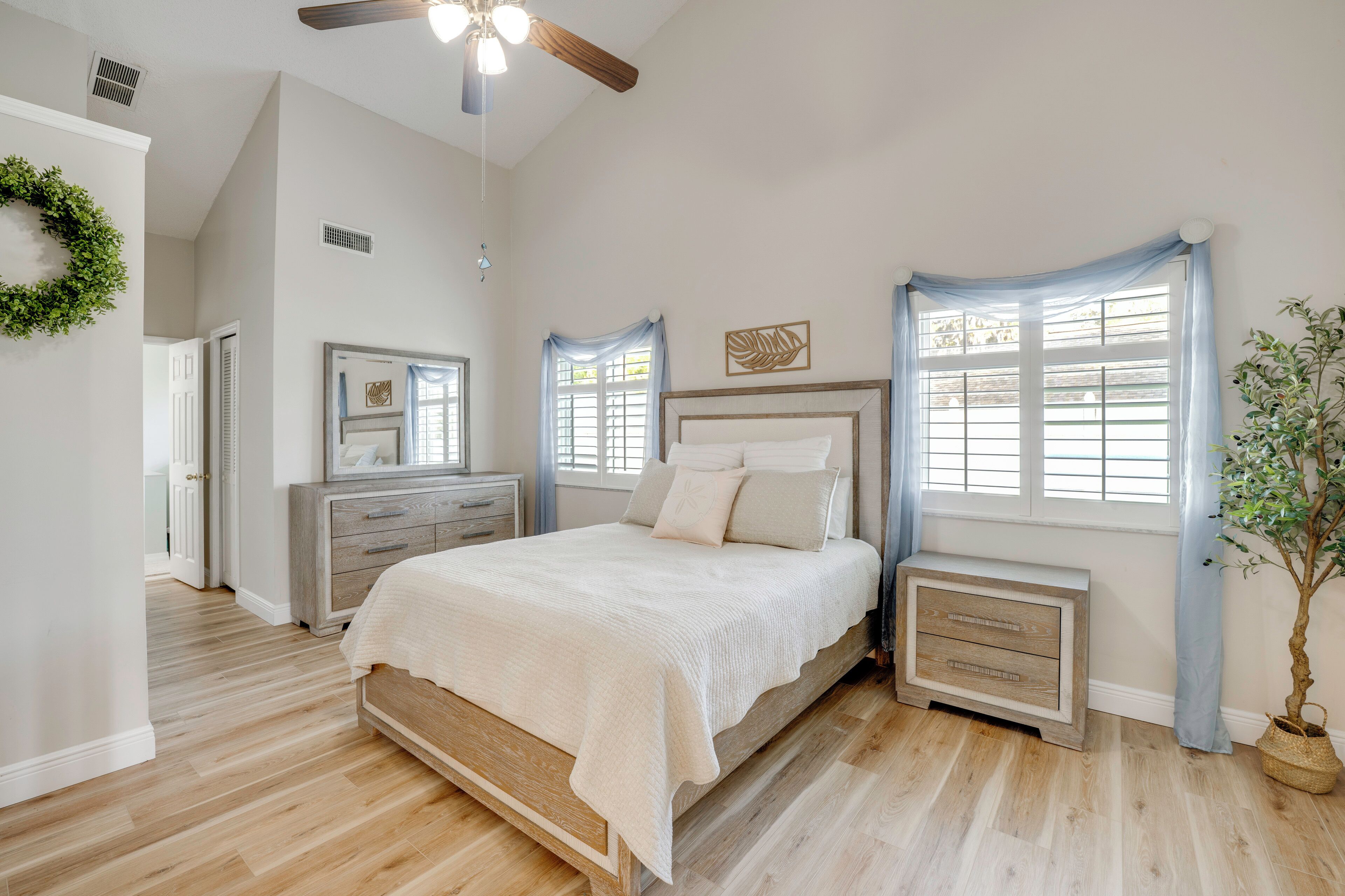 Un dormitorio con cama, cómoda, mesitas de noche, ventilador de techo y ventana con cortinas.