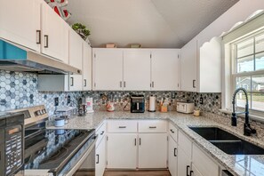 Eine moderne Küche mit weißen Schränken, einer Granit Arbeitsplatte, einem Einbauofen und einem großen Fenster.