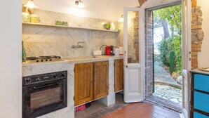 A kitchen with a stove, oven, wooden cabinets, marble backsplash, and a door leading to a garden. - Terrazzina by Interhome (Rosignano Marittimo)