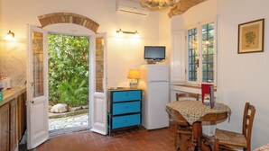 A room with a tiled floor, a wooden table with chairs, a blue chest of drawers, a white refrigerator, a television, and a door leading to a garden. - Terrazzina by Interhome (Rosignano Marittimo)