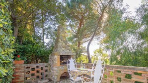 An outdoor patio with a stone oven, metal chairs, and a brick wall. - Terrazzina by Interhome (Rosignano Marittimo)