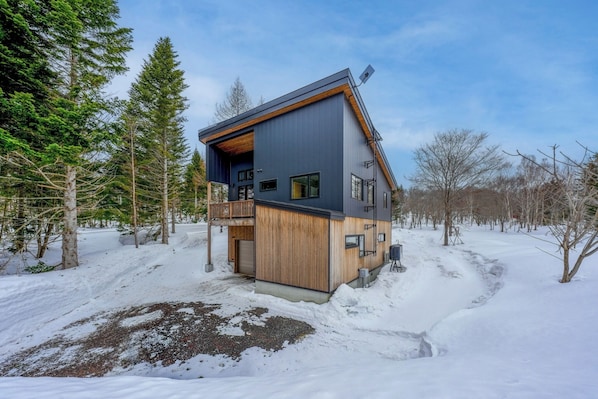 Une maison moderne dotée d’une terrasse en bois, d’un balcon et surplombant un paysage enneigé.