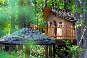 Une cabane dans les arbres avec une terrasse en bois et un toit de chaume.