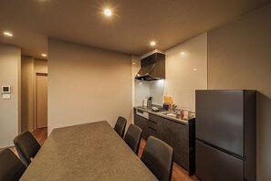 Moderni keittiö, jossa on ruokapöytä ja -tuolit, jääkaappi sekä sisäänrakennettu uuni.