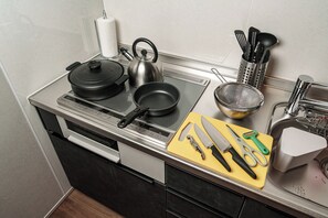 Uma cozinha com fogão, panelas, chaleira, tábua de corte com facas, escorredor e pia.
