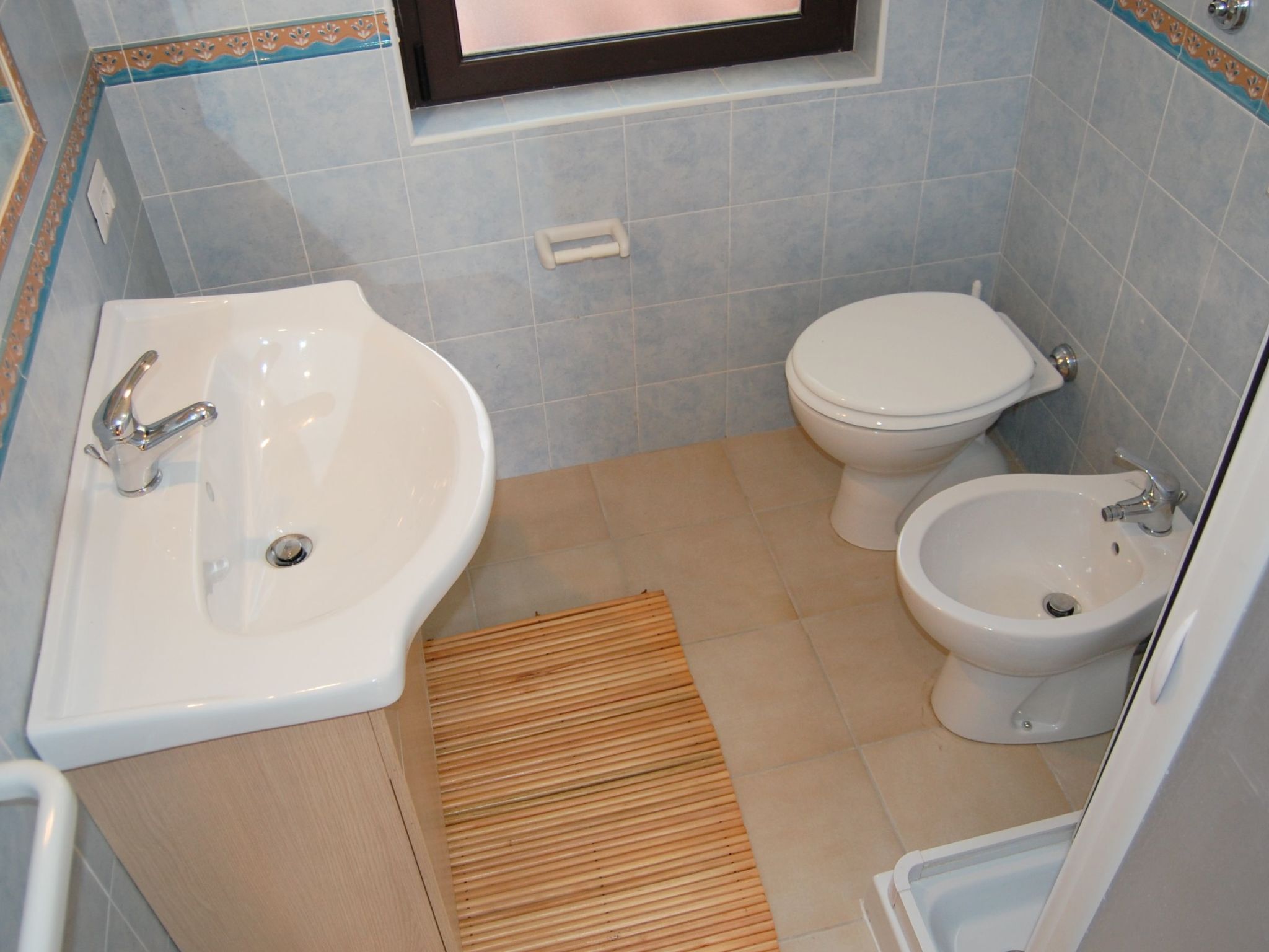 Ein Badezimmer mit Waschbecken, Toilette, Bidet und einer Holzbadematte.