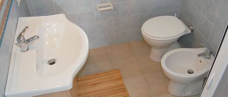 Ein Badezimmer mit Waschbecken, Toilette, Bidet und einer Holzbadematte.