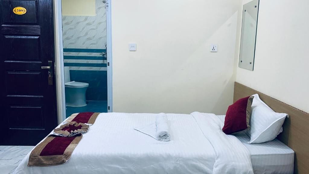 Una habitación de hotel con una cama, un baño a la vista a través de una puerta abierta y un espejo en la pared.