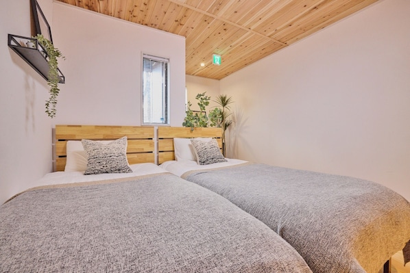 Quarto com duas camas, cabeceiras de madeira, uma janela e uma planta.