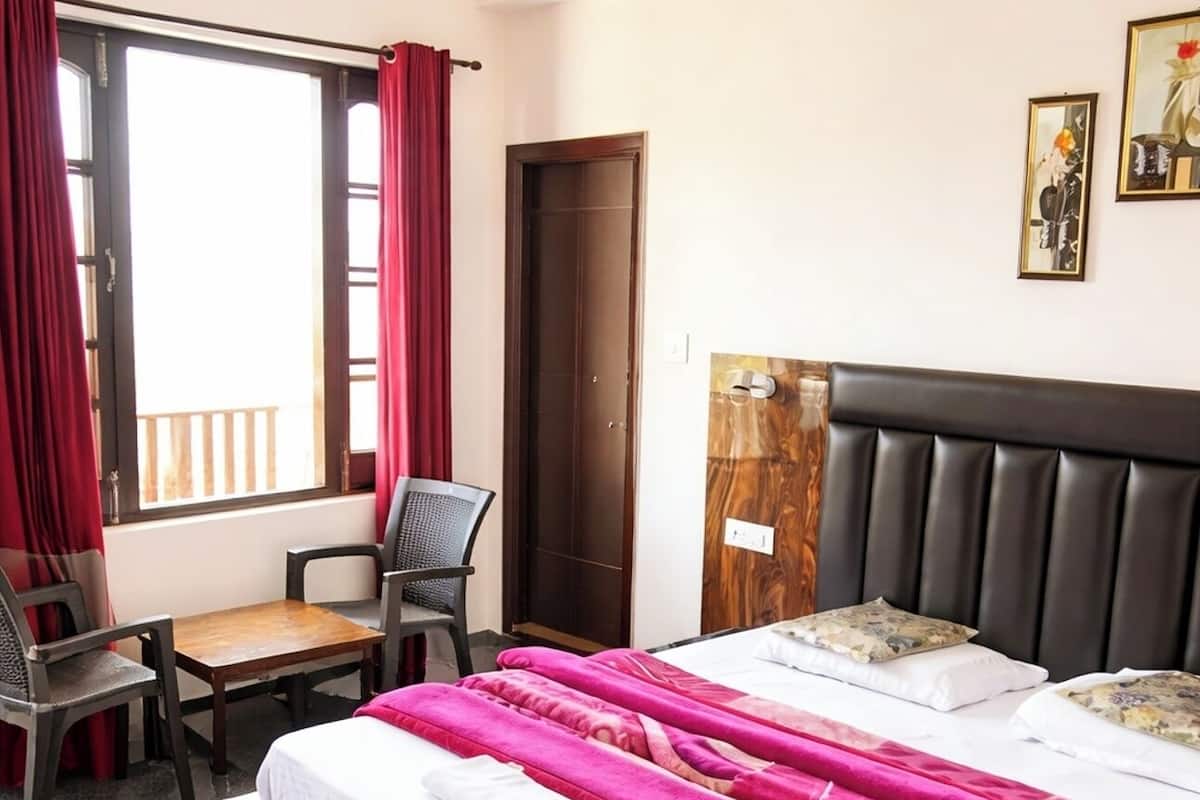 A hotel room with a bed, a desk, a chair, a window with curtains, and a door.