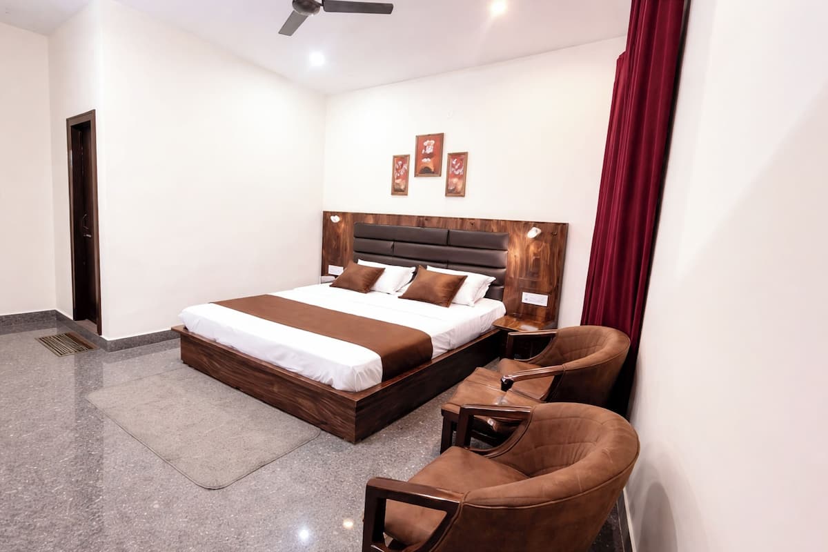 A modern bedroom with a large bed, a wooden headboard, a seating area with chairs, and a ceiling fan.