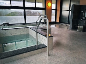 Uima-allas, jonka pohja on lasia, metallinen tikapuut ja näkymä ulkopuolella olevaan rakennukseen.