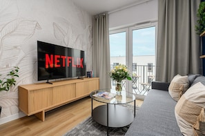Un salon moderne doté d’un grand téléviseur à écran plat, d’un meuble TV en bois, d’une table basse en verre, d’un canapé gris et d’un balcon avec vue.