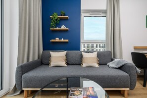 A modern living room with a grey sofa, two cushions, a glass coffee table, and a window with curtains. - Lumina Apart near Orientarium ZOO Łódź (Łódź)