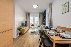 A modern kitchen with wooden cabinets, a dining area with a table set for two, and a balcony with a view. - Lumina Apart near Orientarium ZOO Łódź (Łódź)