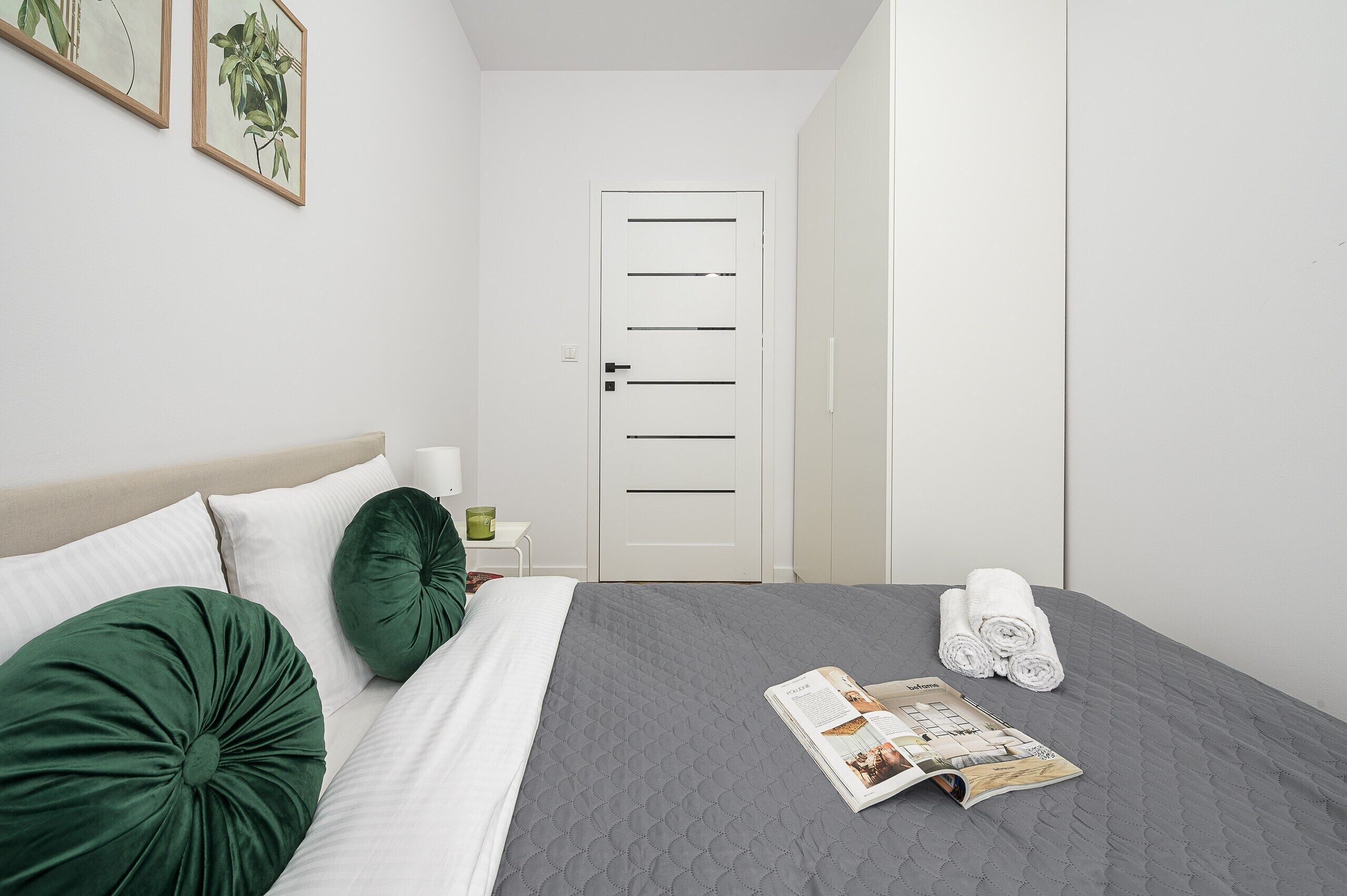 A neatly made bed with green and white pillows, a grey quilt, and a magazine on the bed.