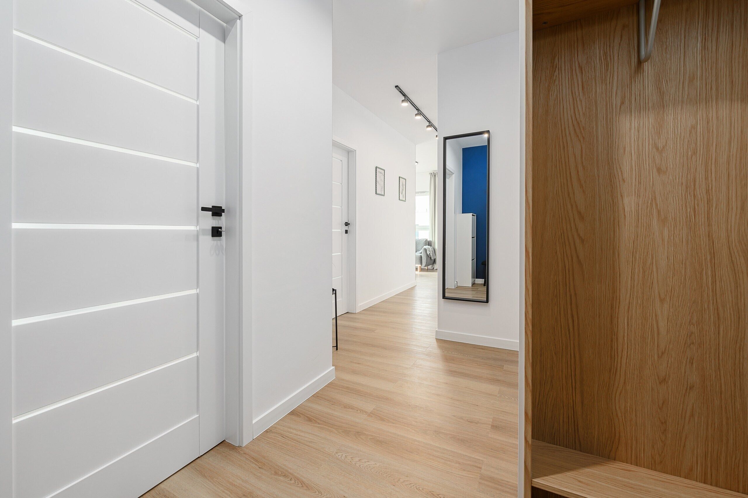 Un couloir avec une porte blanche, un plancher en bois et un miroir accroché au mur.