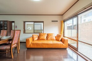 Ein Wohnzimmer mit einer Couch, einem Esstisch mit Stühlen, einem Fenster und einem an der Wand befestigten Garderobenständer.